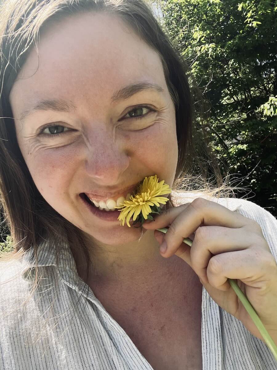 lächelnde Frau probiert eine Löwenzahnblüte