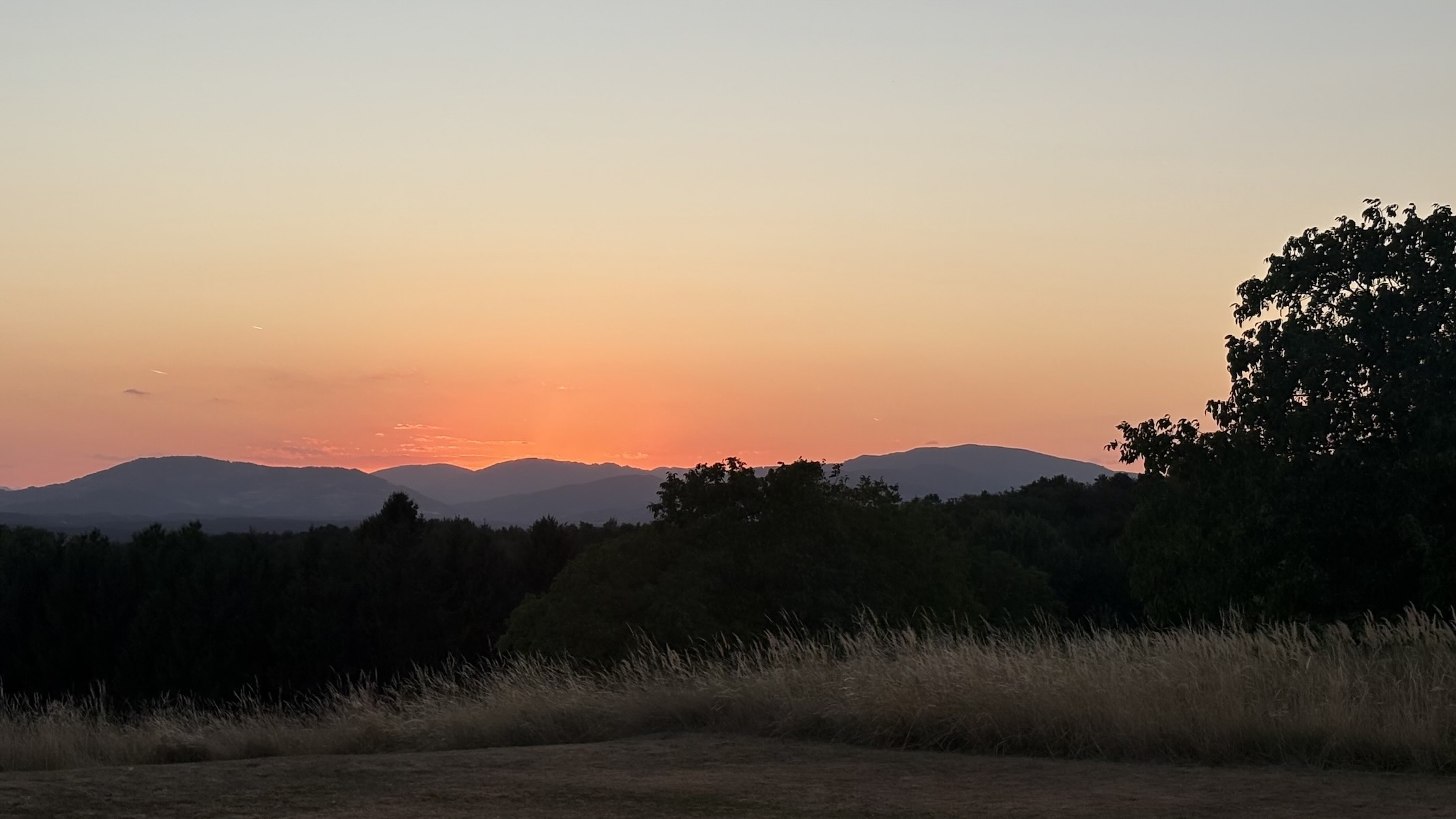 Sonnenuntergang über einer ruhigen Berglandschaft mit Wiesen und Bäumen